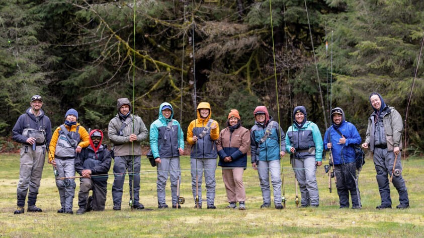 Eleven men and women of color dressed in fishing gear with fishing poles, smiling for the camera. 