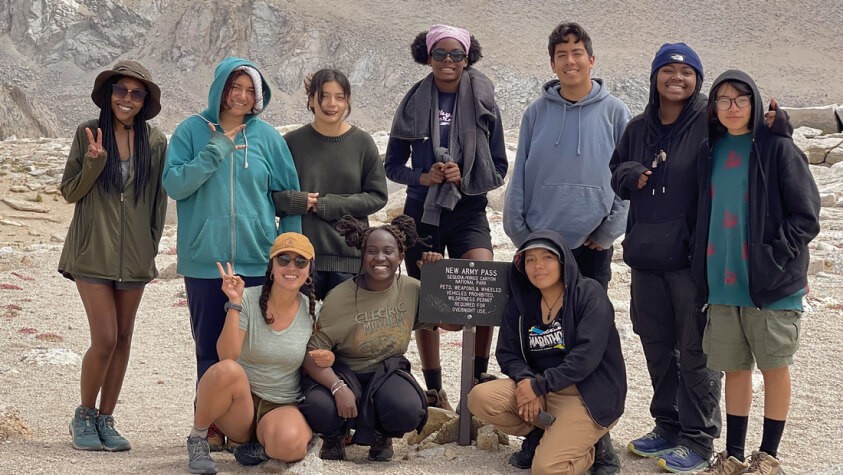 A group of ten diverse youth smiling toward camera while hiking New Army Pass. 