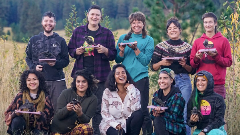A diverse group of ten queer youth smiling while holding taxidermied birds.  