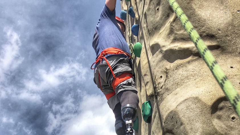 Roped up and reaching toward cloud dappled blue skies, a climber approaches the final grab.