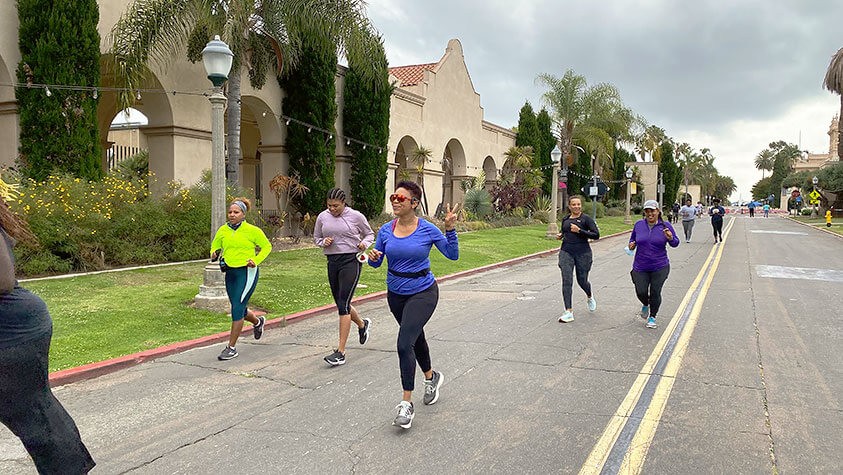 Mid-run in front of palms trees and stucco buildings, participants share peace signs and smiles.
