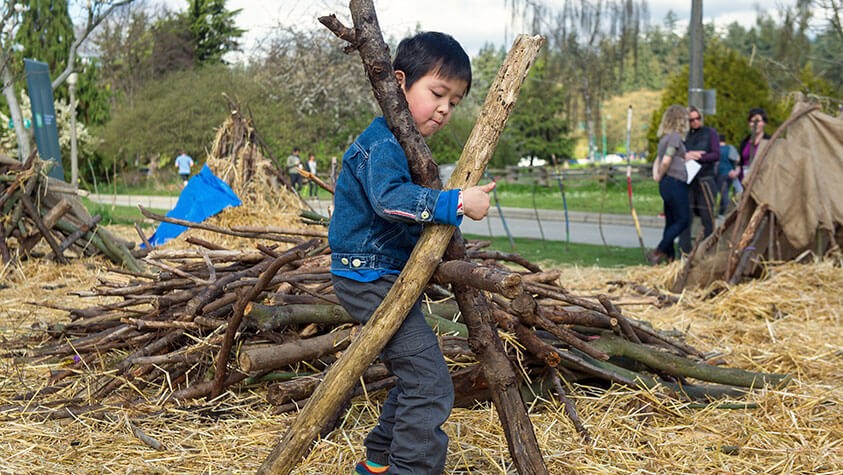 At a suburban park, kids learn to build shelters from branches and straws.