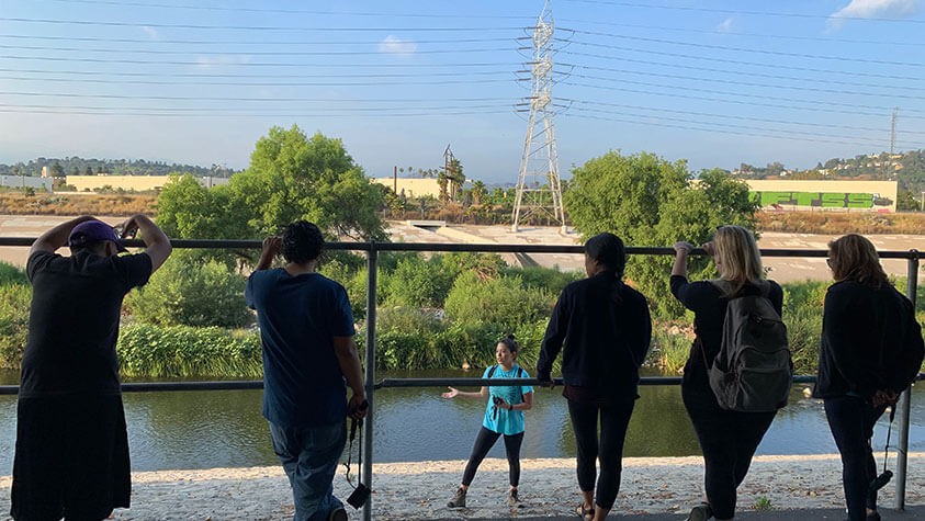 Kids and adults listen to a volunteer explain the benefits of keeping the Los Angeles River clean.