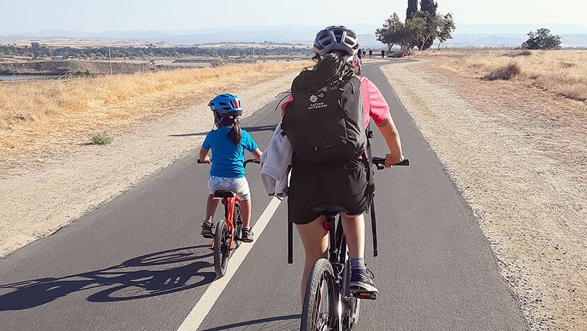 A parent and child enjoy an afternoon ride along a dedicated bike path under sunny California skies.