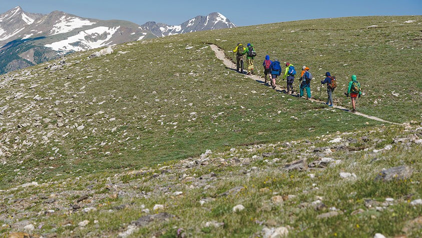 Single file along an alpine path, a group of spring hikers head toward their snow dappled destination.