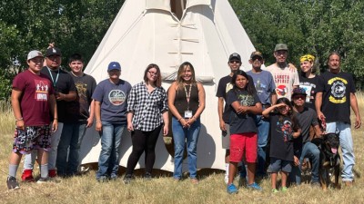 A group of Lakota youth standing with two elders in front of a white Tipi