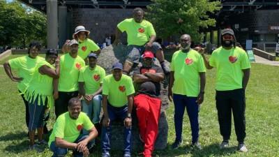 A group of smiling Black people surrounding a large boulder while wearing bright green Friends of Anacostia shirts.