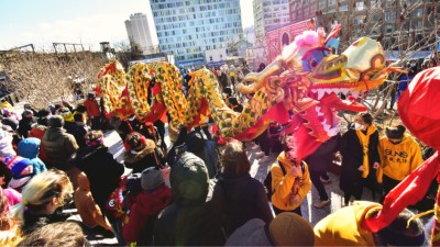 A group of people in mittens and cozy jackets watch as a dragon puppet dances during Chinese New Year. 