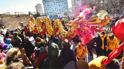 A group of people in mittens and cozy jackets watch as a dragon puppet dances during Chinese New Year.