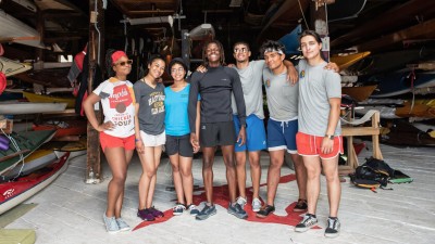 A diverse group of seven college-aged people standing in front of a boat storage room.