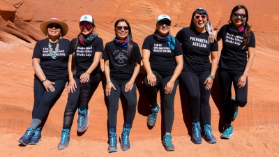 Six Native women smiling in front of red sedimentary rock. 