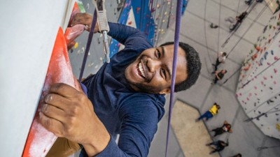 A man smiles as he scales a wall in a climbing gym