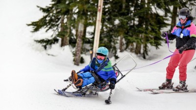 Two people alpine skiing, one using a bi-ski 