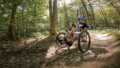 A man rides an adaptive bicycle on a wooded trail