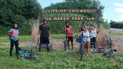 A group of friends and their bikes pause for a photo under the City of Chicago Big Marsh Park sign.