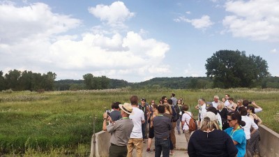 Standing on a boardwalk, with cameras and binoculars, a group ov visitors admire protected river wetlands.
