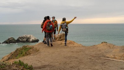 Four dayhikers stand above a seaside cliff, greeting the limitless expanse of the Pacific Ocean.