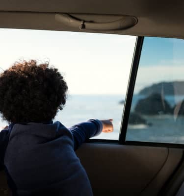 A child points excitedly out a car window at the surf of the Pacific Ocean far below.