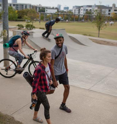 Two friends enjoy a stroll, a cyclist heads to yoga and a skateboarder all enjoy their city park.