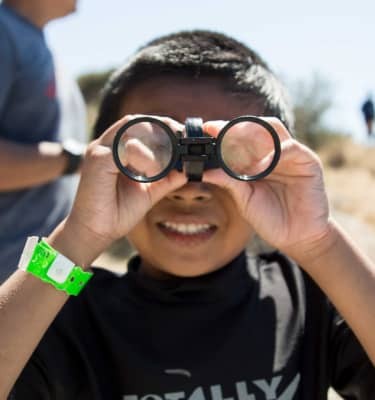 I Spy! Binoculors help a young camper explore the sand dunes of a national park.