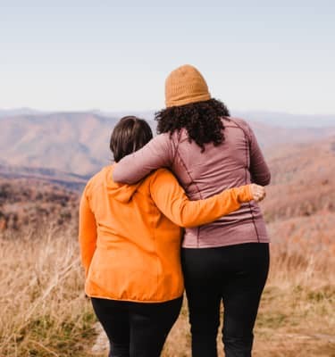 Sharing a hug and the view, two hikers pause to take in the expanse of autumn tinged hills fading into the distance.