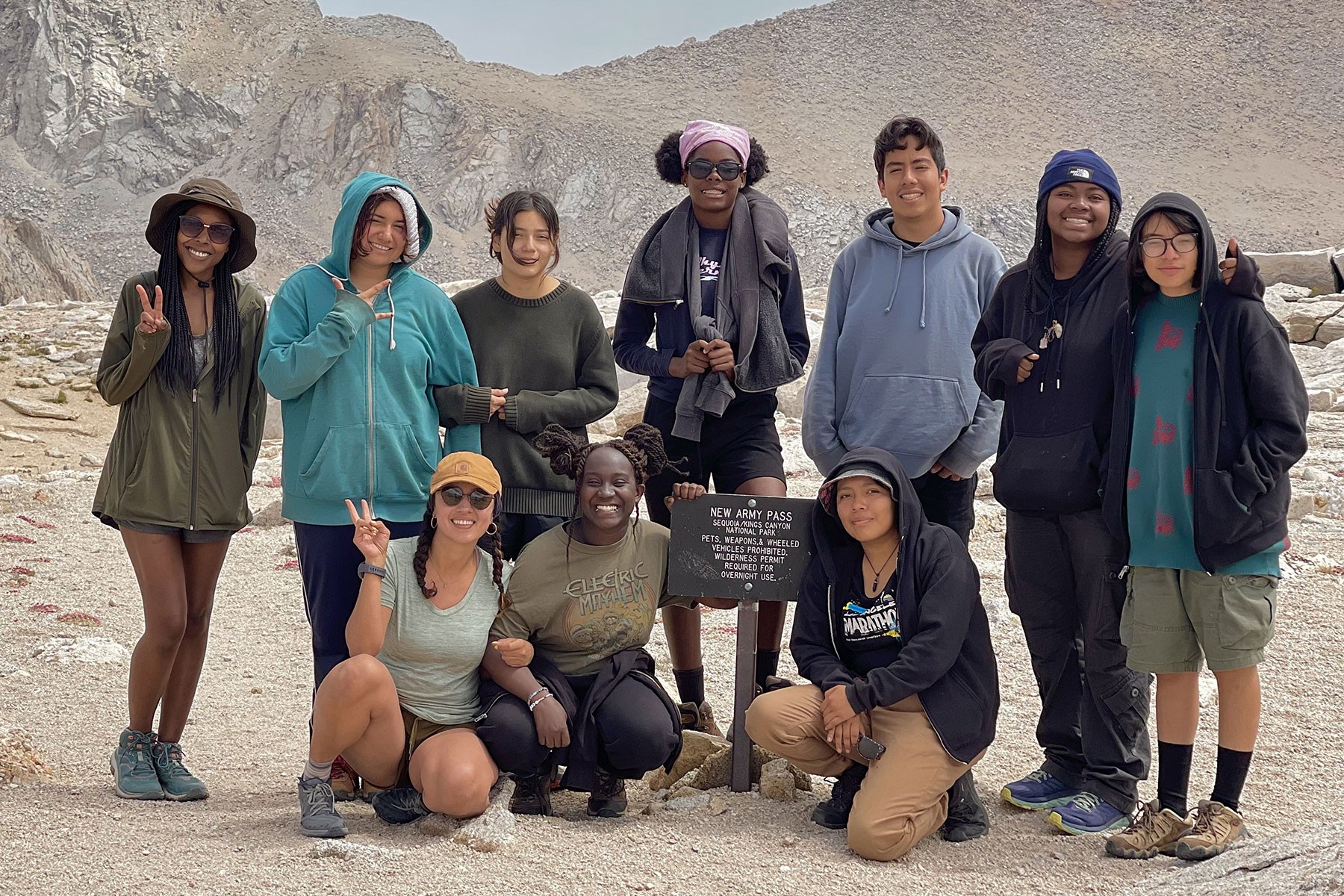 A group of ten diverse youth smiling toward camera while hiking New Army Pass. 