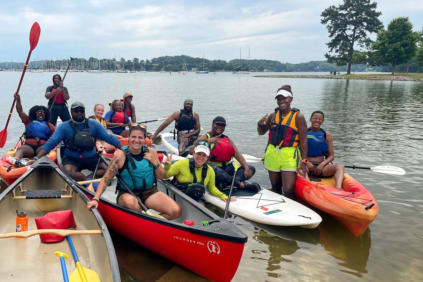 A diverse group of twelve people wearing swimsuits and swim shorts while sitting in boats with paddles in hand along the Tennessee RiverLine