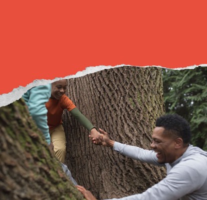 All smiles, a child helps an adult climb a woodland tree.